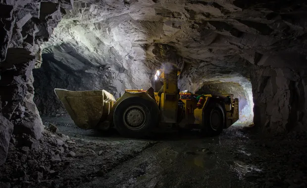 En lastmaskin arbetar i en upplyst gruvtunnel under jord. Den steniga tunnelmiljön och maskinen visar arbete inom gruv- och bergsindustrin.