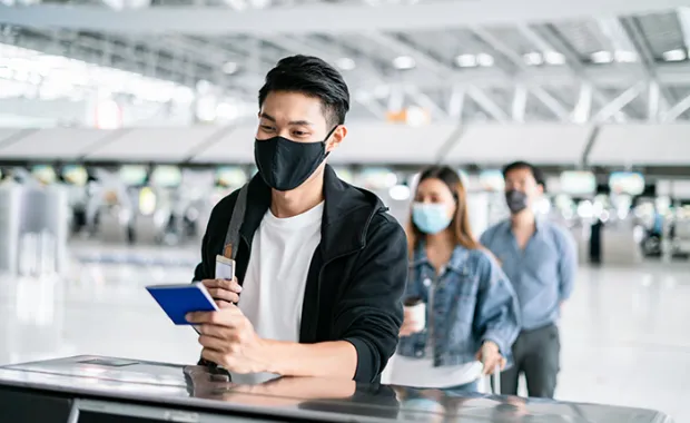 man in a mask holding his passport at a counter 