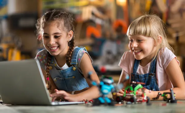 two girls smiling looking at a laptop
