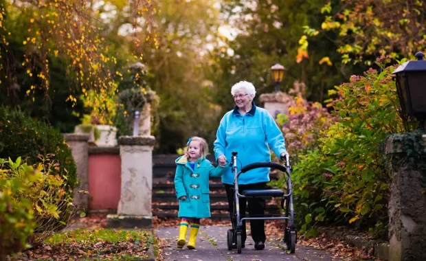 An older woman using a walking frame holds hands with a young girl