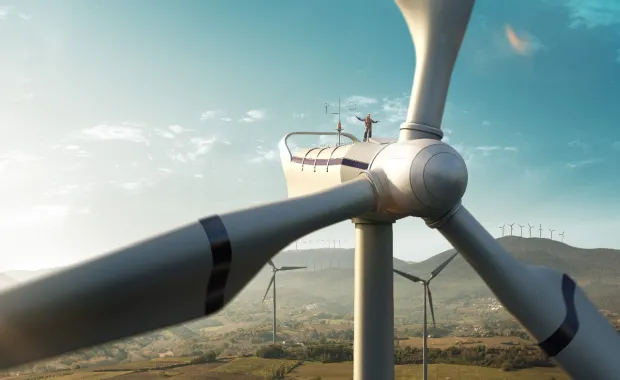 man stands on a wind turbine with more turbines in the landscape in the background