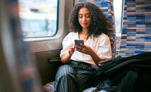 A woman sitting in a patterned train seat by the window using her smartphone