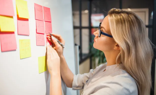 Beraterin steht vor einem Whiteboard mit rot-gelben Post-it und notiert etwas