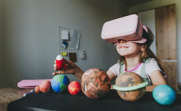 Young girl surrounded by models of planets uses VR headset