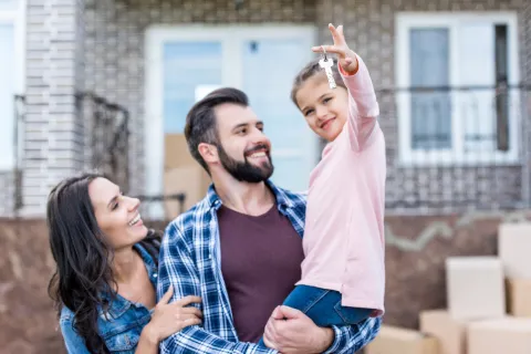 A man and woman smiling at their child who is holding the keys to their home