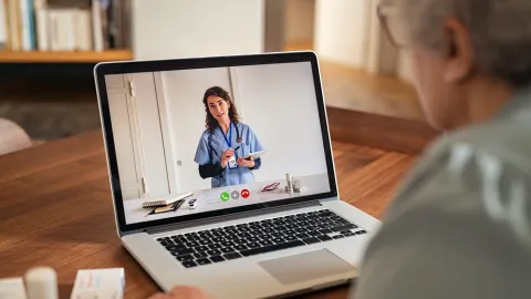 Elderly patient talks to doctor on video call on laptop