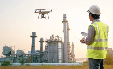 Drone in flight Drone in flight being operated by male professional wearing high vis jacket and helmet