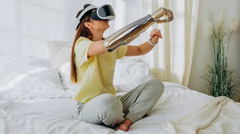 Lady with prosthetic arm sat on bed using VR headset