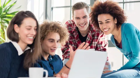 Eine Gruppe junger Personen schaut auf einen Laptop und lachen