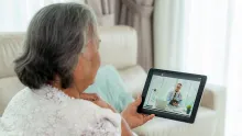 Äldre kvinna sitter hemma och pratar med sin läkare vid surfplatta