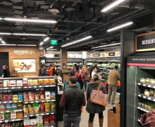 Bild inifrån Amazon Go butik med människor som går runt och shoppar, i förgrunden syns en hylla med mat 