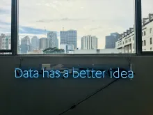 En skylt med neonbokstäver som bildar texten Data has a better idea är uppsatt på en låg vägg nedanför stora fönster som visar en storstadsvy med höghus