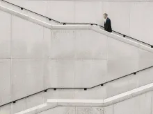 En man i mörk kavaj och vit skjorta går i en vit stentrappa som syns över hela bilden 