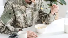 Man i militärkläder sitter vid ett vitt matsalsbord och äter