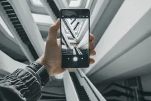 Närbild på en hand som håller i en smartphone och vi ser rulltrappor i en stor och ljus lokal genom kamera i telefon 