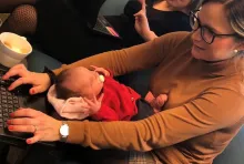 Föräldralediga Michaela Wåhlberg sitter med sin sovande bebis i knät och skriver på sin laptop 