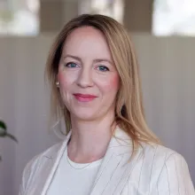 Porträtt av en kvinna med ljust hår som bär en ljus kavaj och ser in i kameran. Bakgrunden är mjukt suddig, vilket ger bilden ett professionellt och välkomnande uttryck.