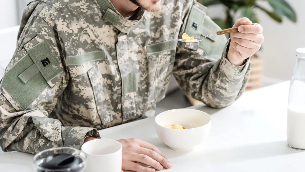 Militärklädd man sitter vid ett vitt matsalsbord och äter mat