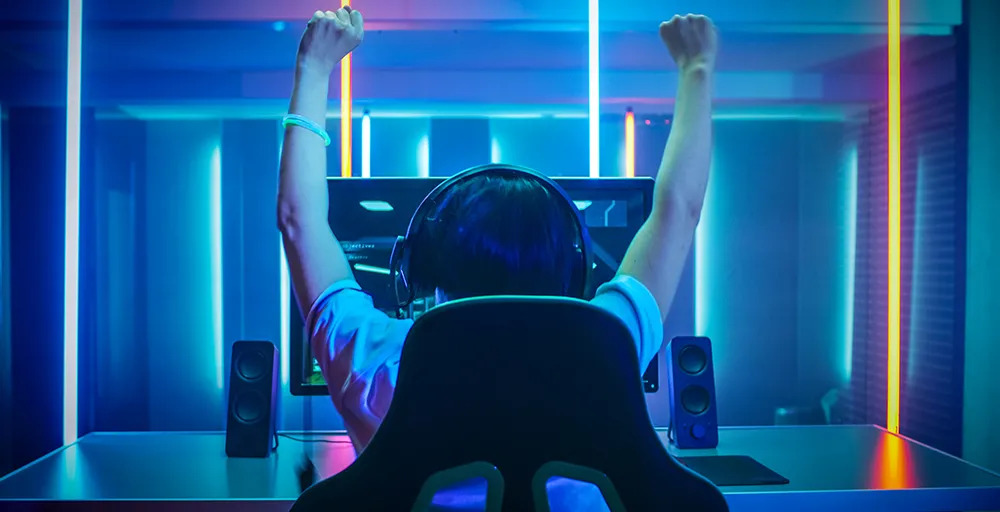 En person höjer armarna i segergest över huvudet vid framgång i e-sport matchen på sin skärm