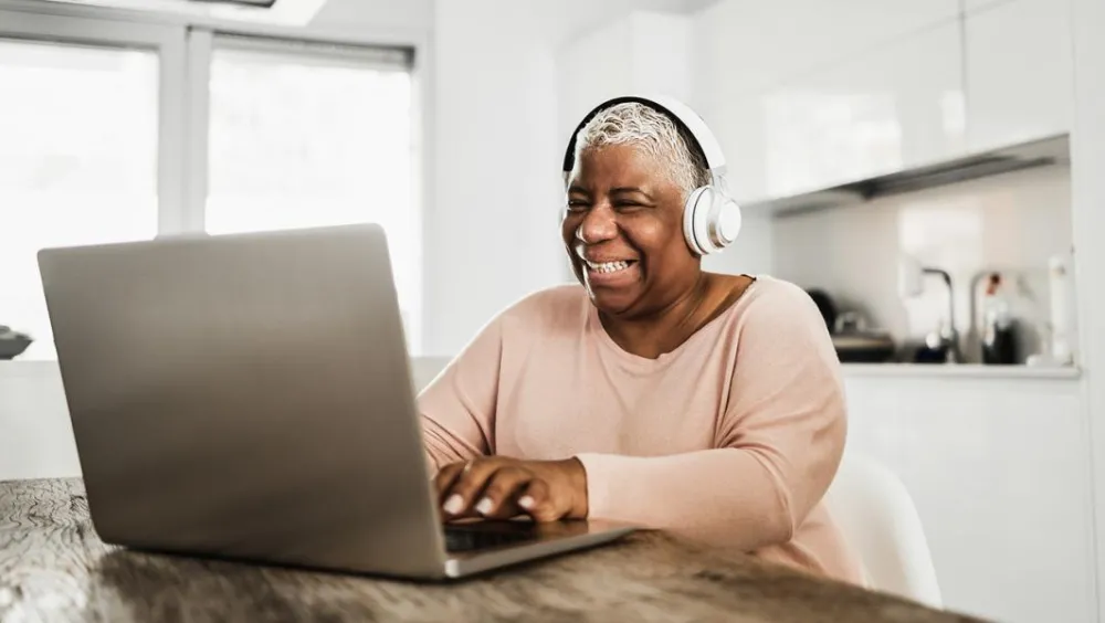 woman sitting in kitchen using laptop wearing white headphones