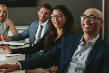 Four business people smiling while listening to a speaker