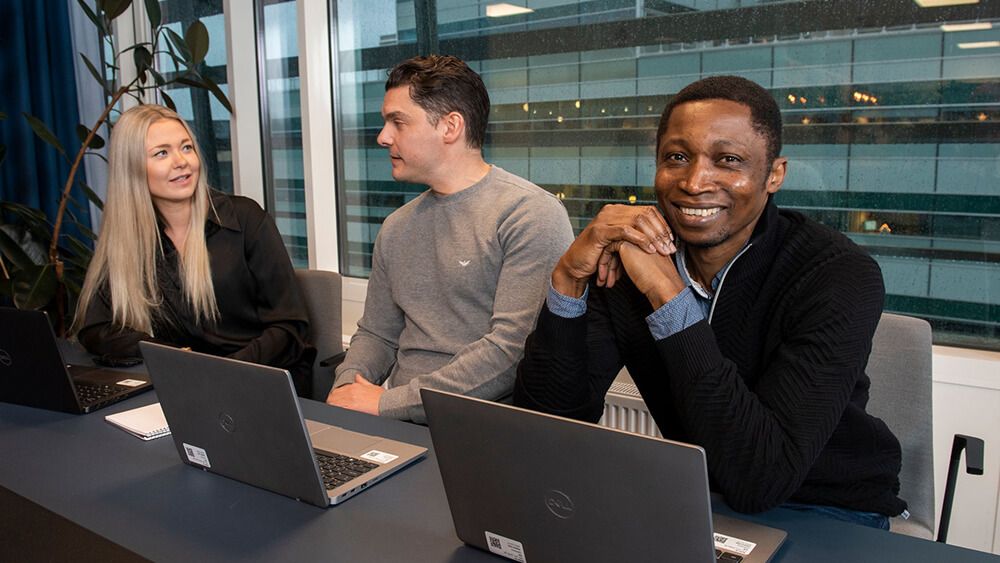 Tre kollegor som sitter på rad vid ett bord med sina laptops