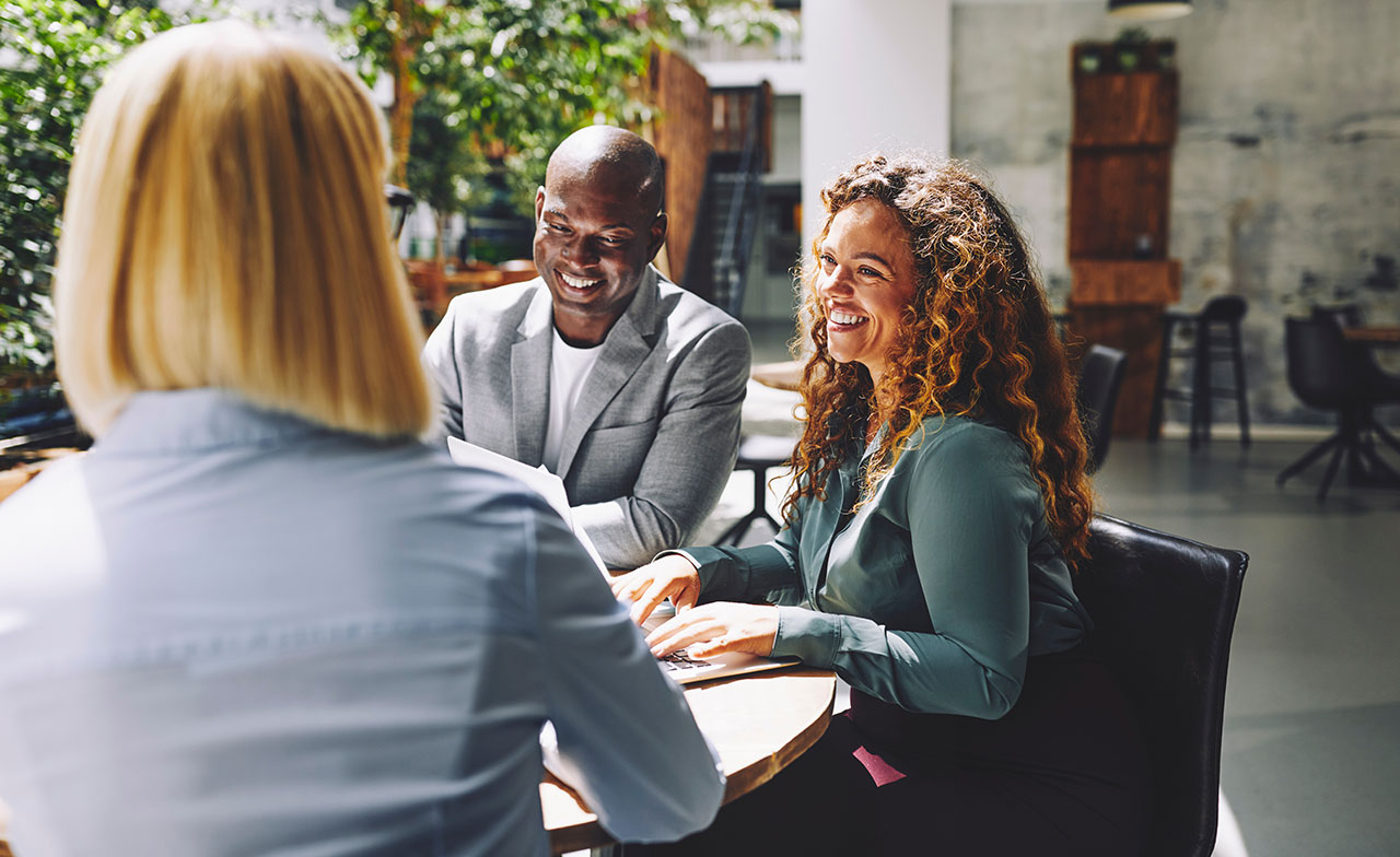 Tre kollegor runt ett bord i en stor ljus samlingslokal