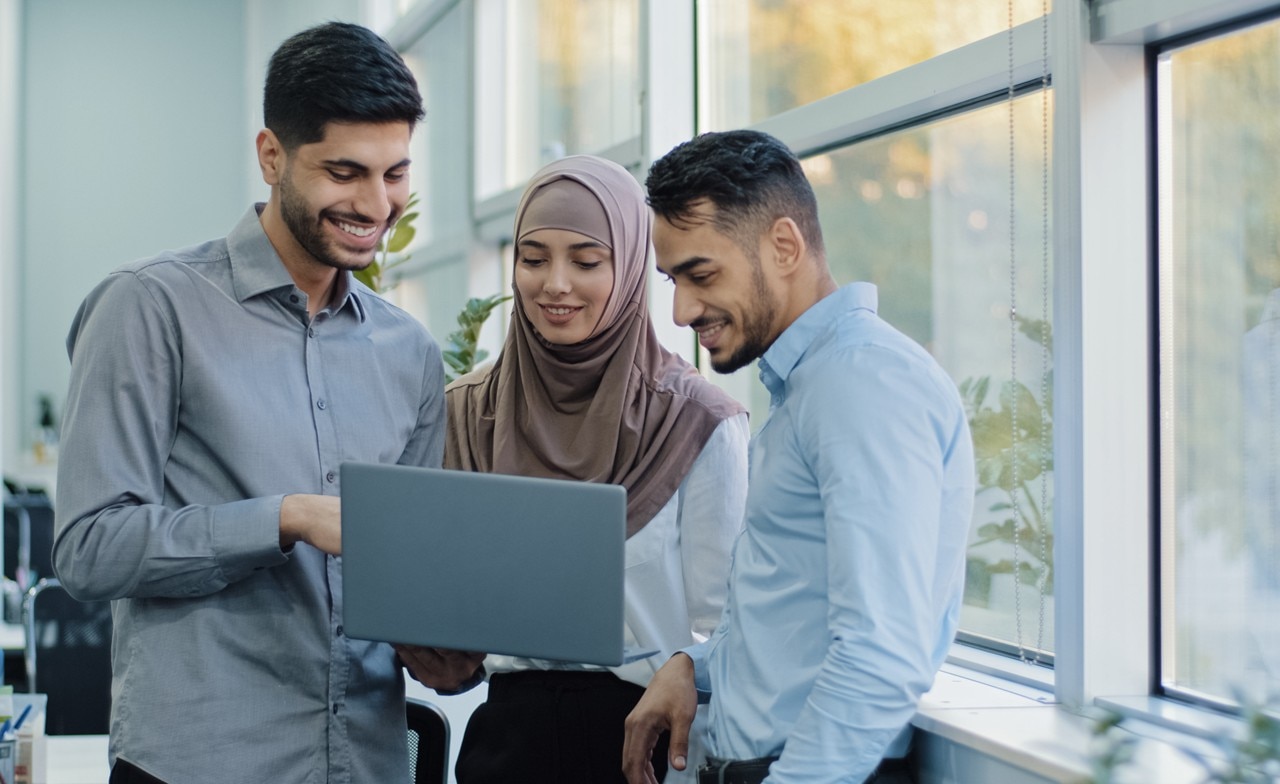 Three colleagues standing in discussion about something on the laptop being held