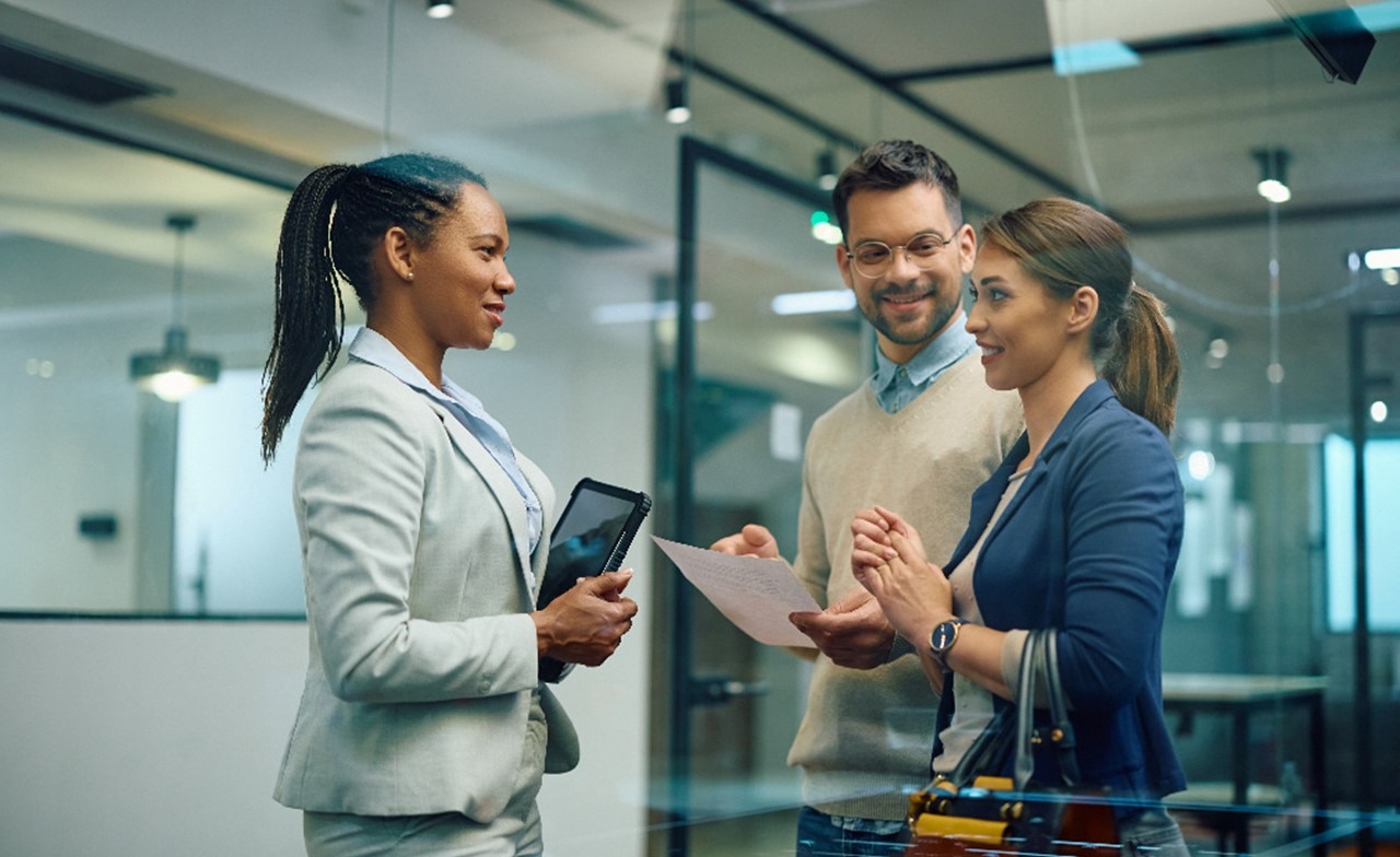 Three professionals in a modern office discussing a document 