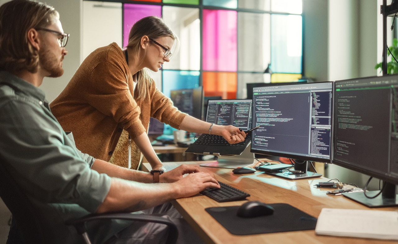 To personer samarbeider foran skjermer med programkode.