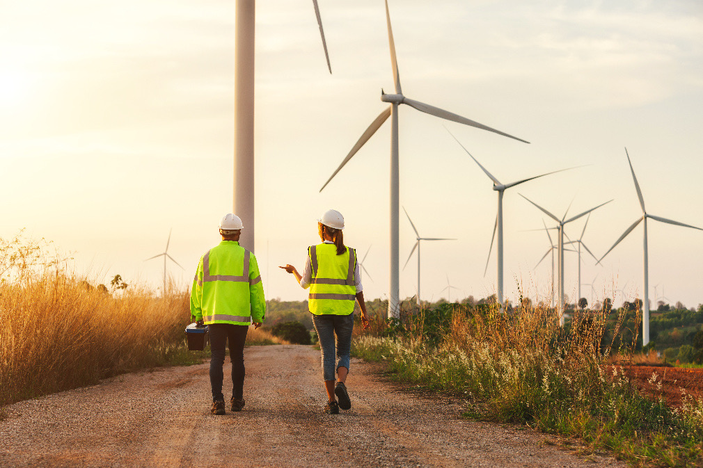 two engineers walk alongside wind turbines in a field