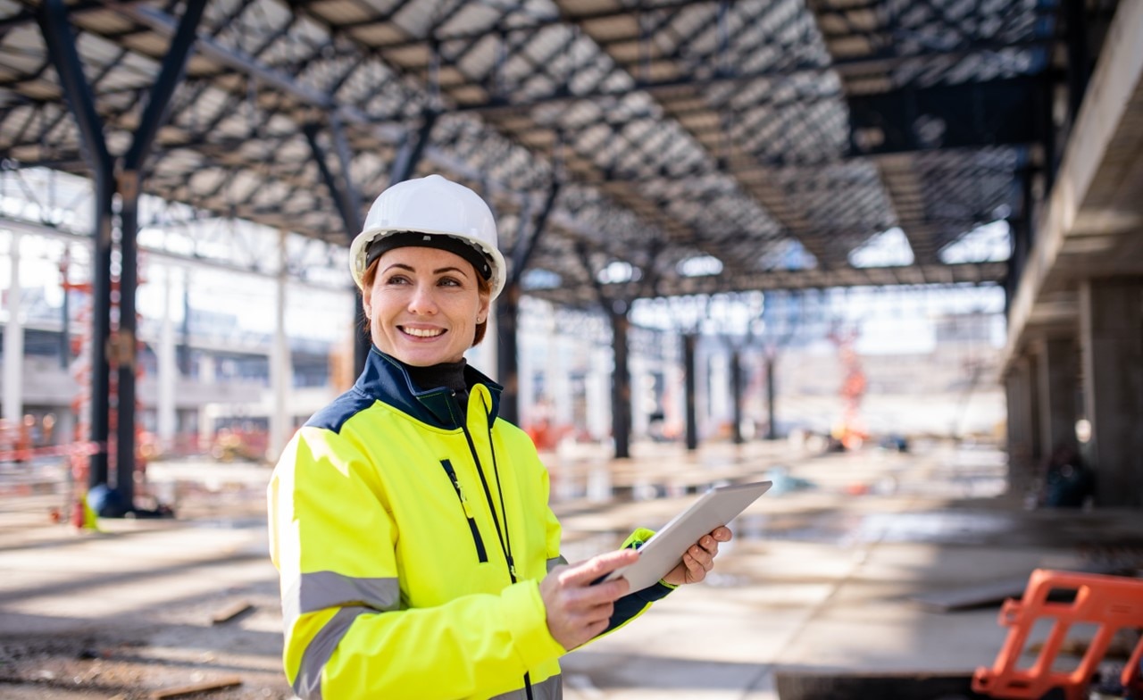 Woman engineer in white hard hat holding laptop at a construction