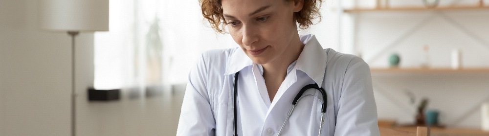 Kvinnlig läkare med stetoskop runt halsen sitter på sitt kontor och tittar på sin surfplatta med patientdata