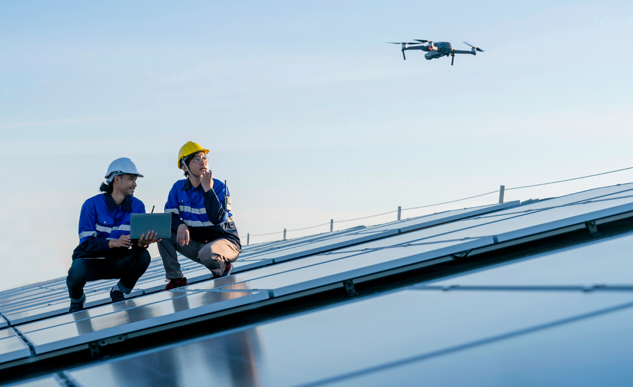 Zwei Techniker kontrollieren eine Drohne, die über eine Photovoltaikanlage fliegt