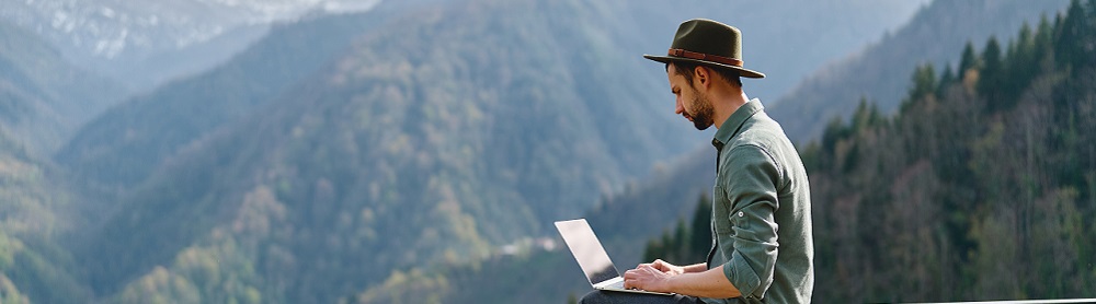 Man sitzt auf der Spitze eines Berges und arbeitet mit seinem Laptop