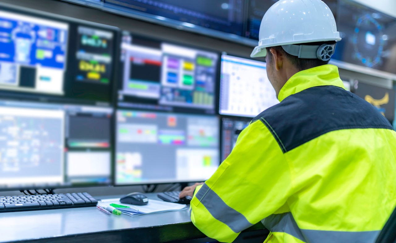 person-yellow-jacket-white-hardhat-working-at-computer-screen Person wearing a yellow jacket and white hardhat monitoring computer data