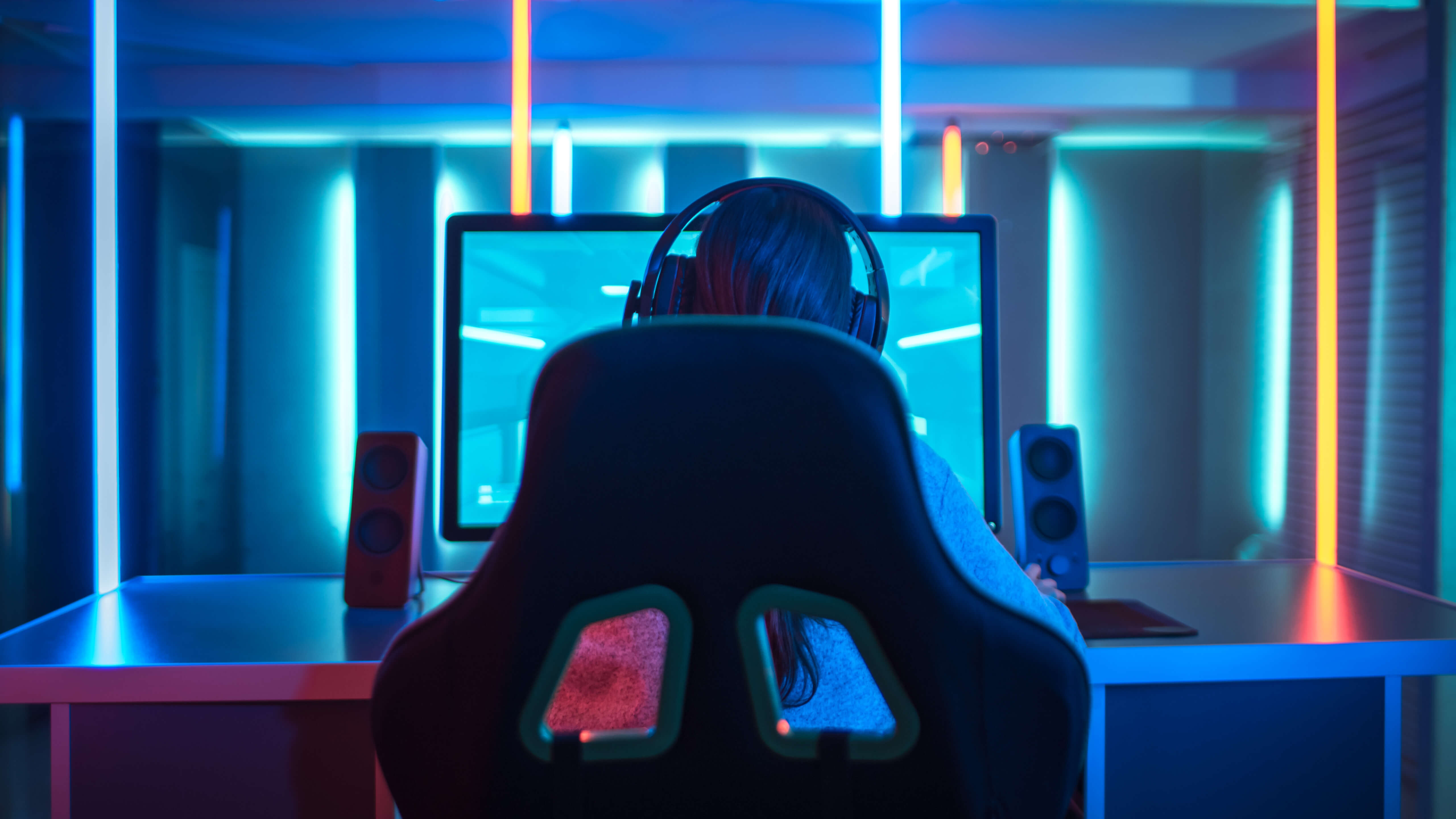En kvinna i ett rum med blått ljus som sitter i en gaming stol framför en stor skärm