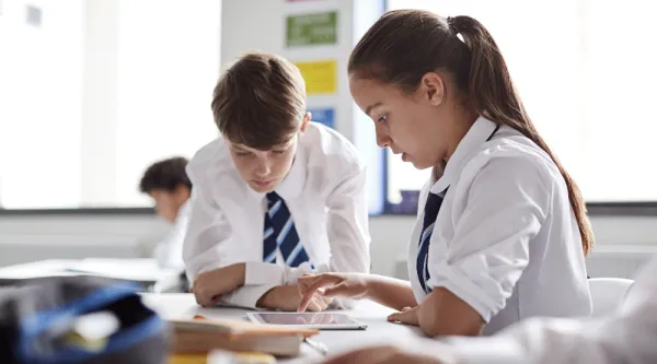two school children in uniform work together on tablet device