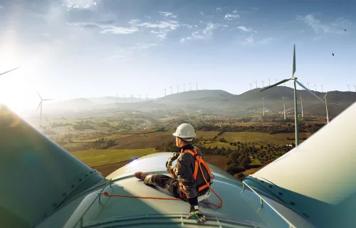 engineer sitting atop a wind turbine looking at a sunset landscape