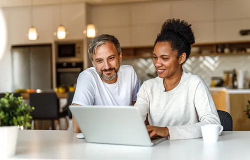 a man and a woman working on their computer in the kitchen