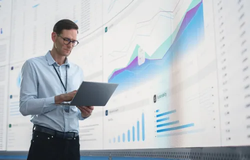 data analyst looking at a tablet in front of a large screen