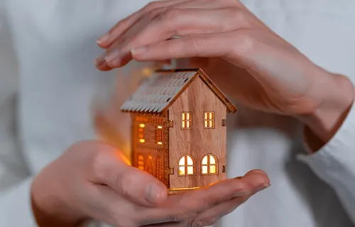 person holding a lighted model of a wooden house