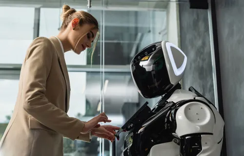 Une femme en blazer interagit avec un robot humanoïde dans un bureau.
