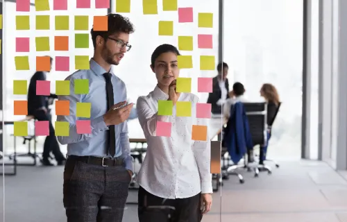 Zwei Consultants stehen vor einer gläsernen Post-it Wand