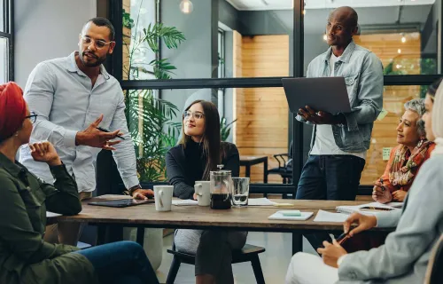 office meeting with particpiants engaged in conversation around a wooden table