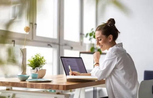 smiling woman at desk with laptop and pen and notepad