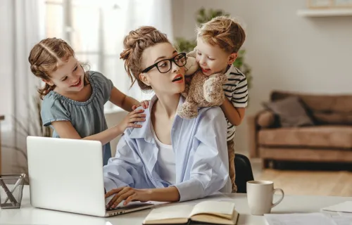 Parent at computer speaking with children over her shoulder