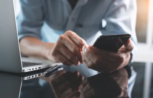 Personne devant un ordinateur regardant un téléphone portable.