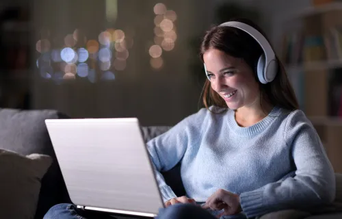 A smiling person wearing headphones looking at a laptop