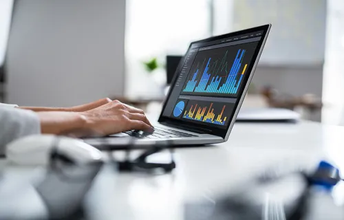 Två händer som skriver på en laptop som visar diagram och data